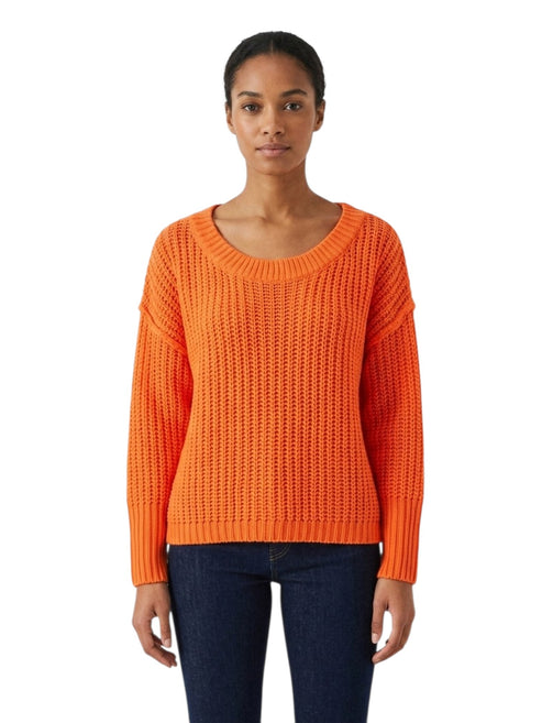 A woman modeling a bright orange textured knit sweater with a wide scoop neckline and long sleeves, paired with dark blue jeans, against a plain white background.