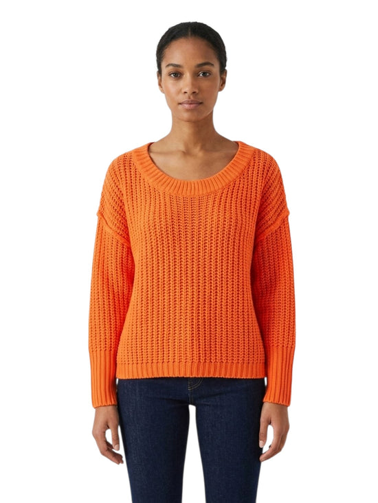 A woman modeling a bright orange textured knit sweater with a wide scoop neckline and long sleeves, paired with dark blue jeans, against a plain white background.