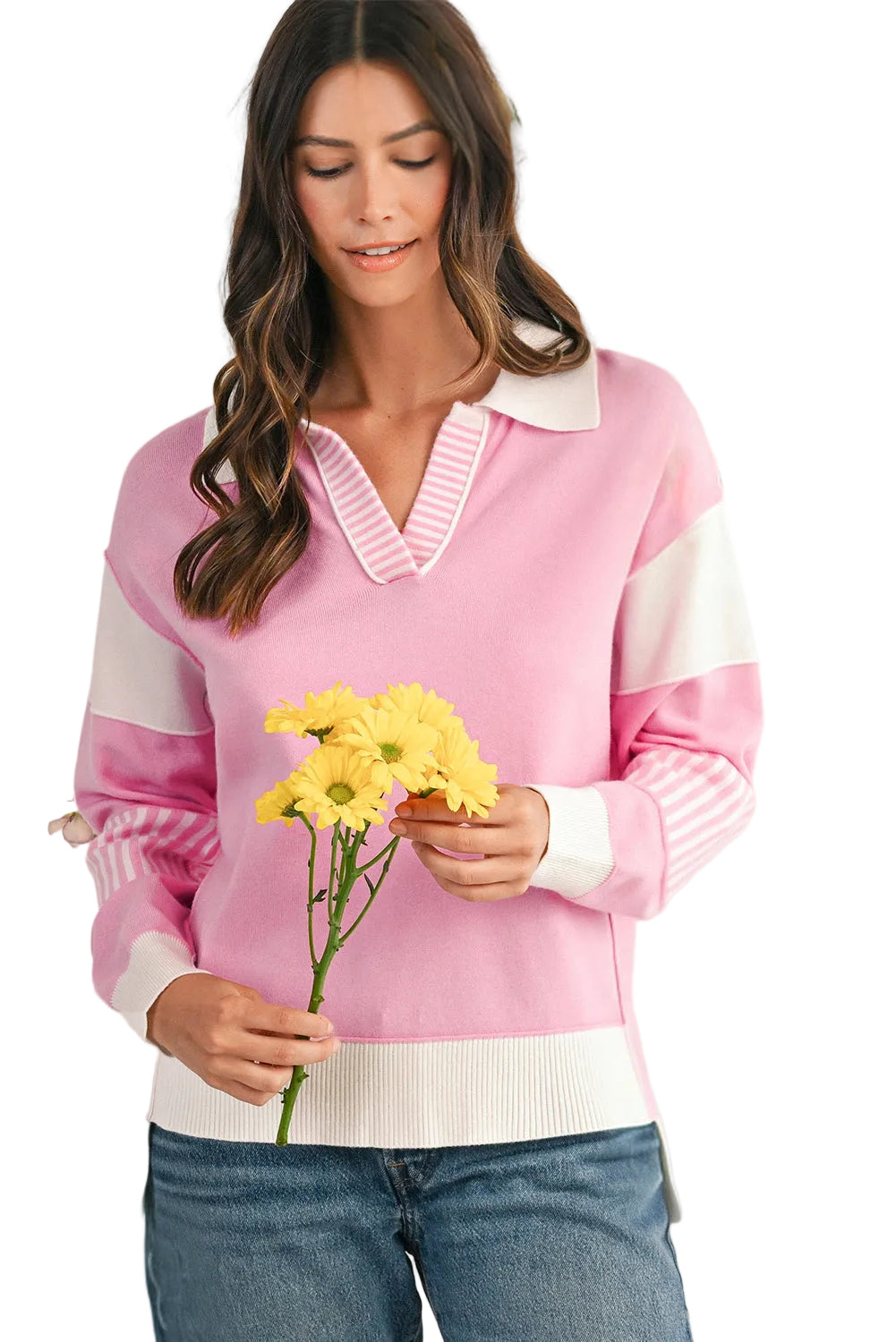 Woman wearing a pink and white sweater holding yellow flowers against a white background