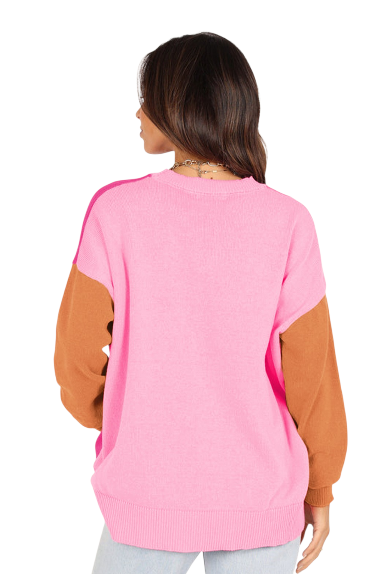 The back view of the woman wearing the color-block sweater. The back panel is a solid light pink, contrasting with the warm caramel brown sleeves and the magenta hints visible at the shoulders. The sweater features a wide ribbed hem for a cozy finish.