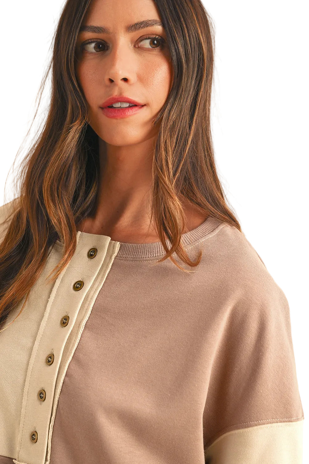 Woman wearing a beige and brown top with a neutral background