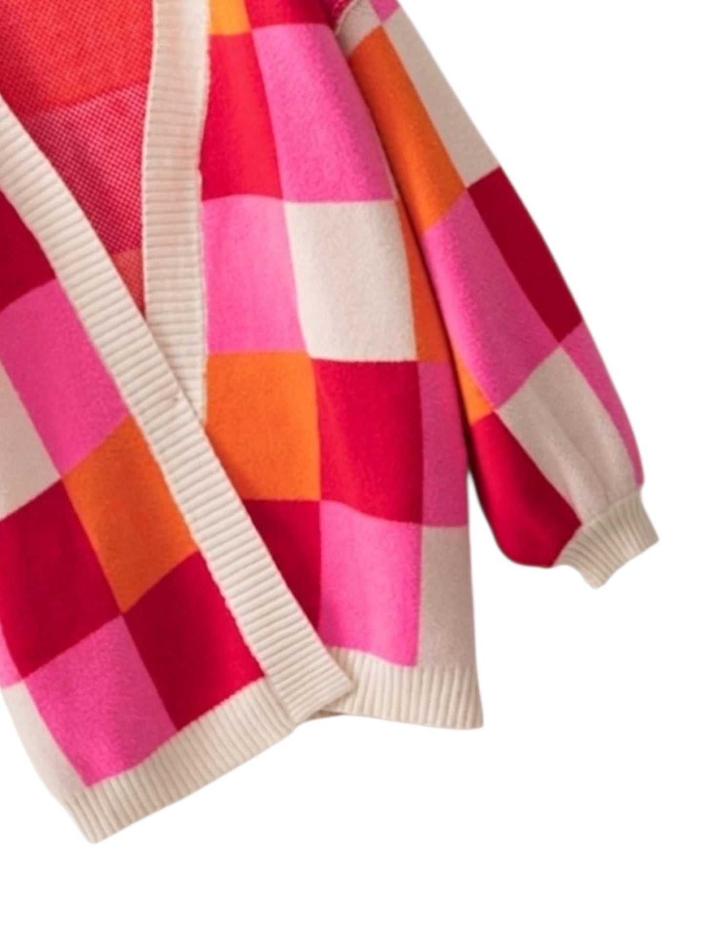 A close-up of a knit cardigan with a colorful patchwork check pattern in pink, red, orange, and cream, featuring cream ribbed trim.