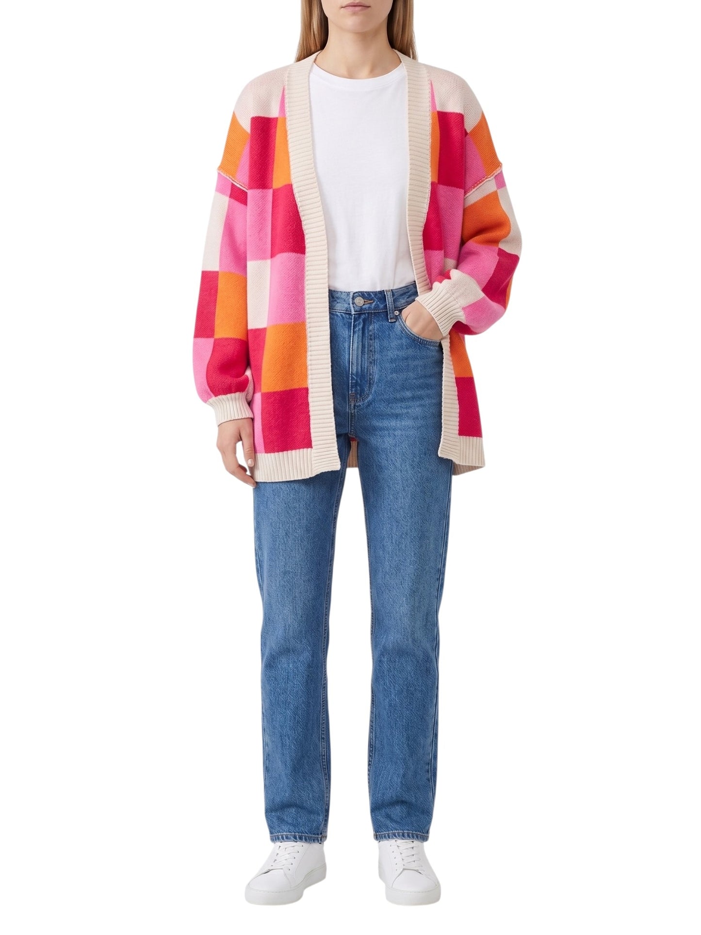 A model wearing a colorful patchwork knit cardigan with pink, orange, and cream blocks over a white t-shirt, blue jeans, and white sneakers, shot against a plain white background.
