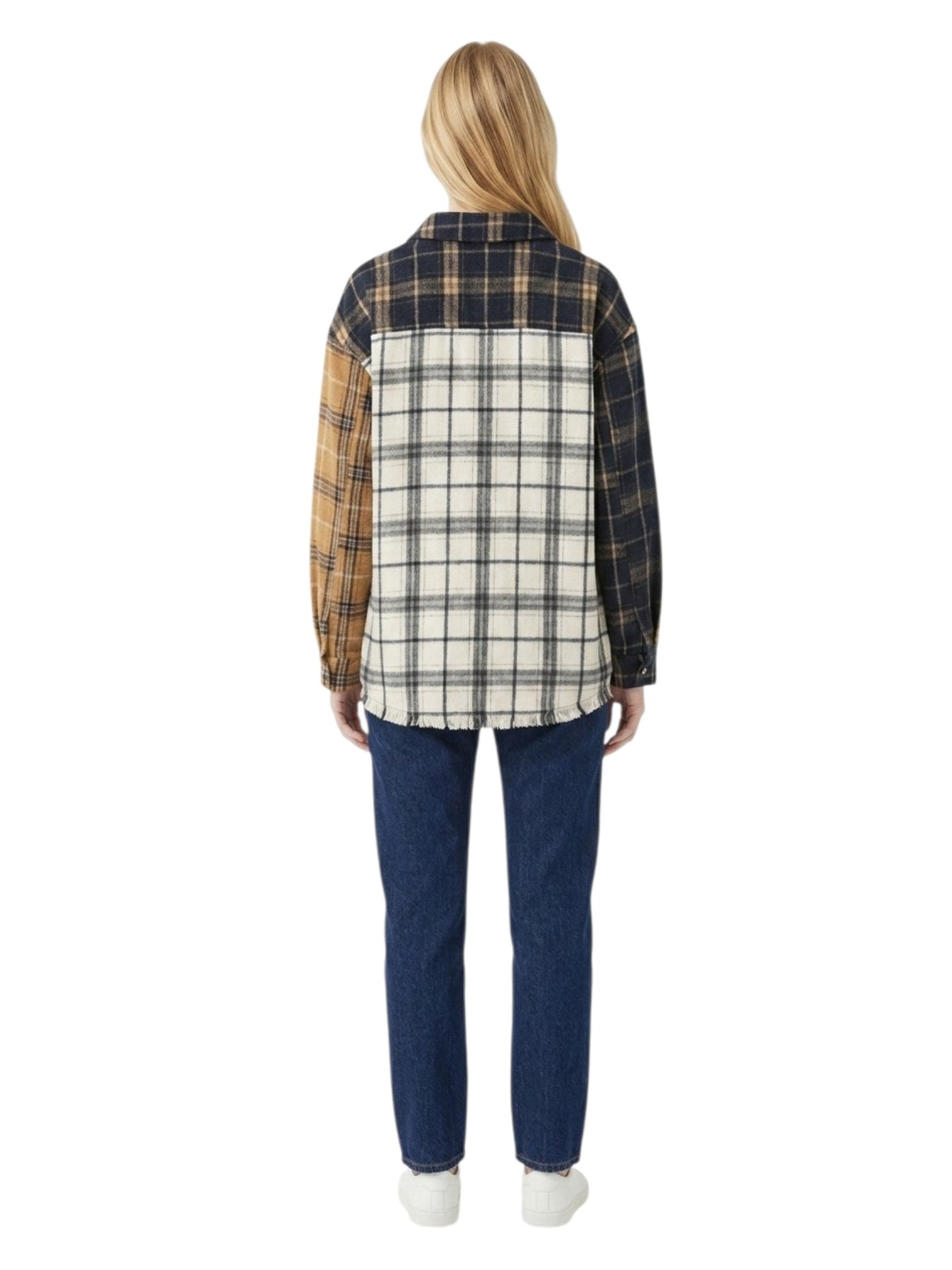 A woman viewed from the back wearing a patchwork plaid flannel shirt with navy, tan, and cream panels, paired with blue jeans and white sneakers, on a solid white background.