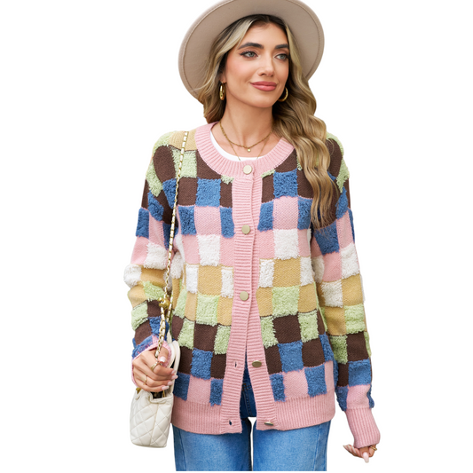 A woman wearing a modern colourblock plaid cardigan featuring textured pink, blue, brown, and olive green squares with gold-toned buttons.