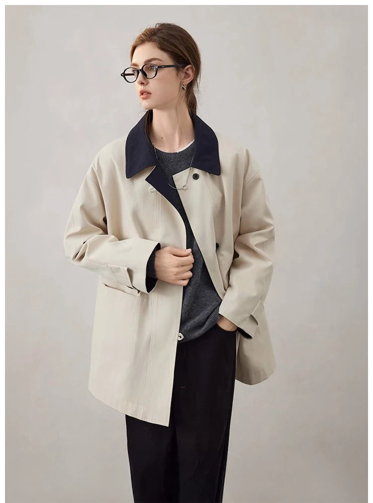 Person wearing a beige coat with a dark collar against a plain background