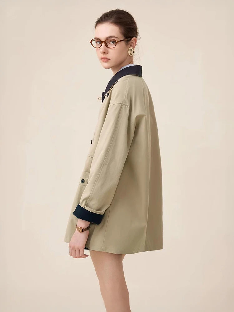 Woman wearing a beige trench coat with navy trim on a plain background