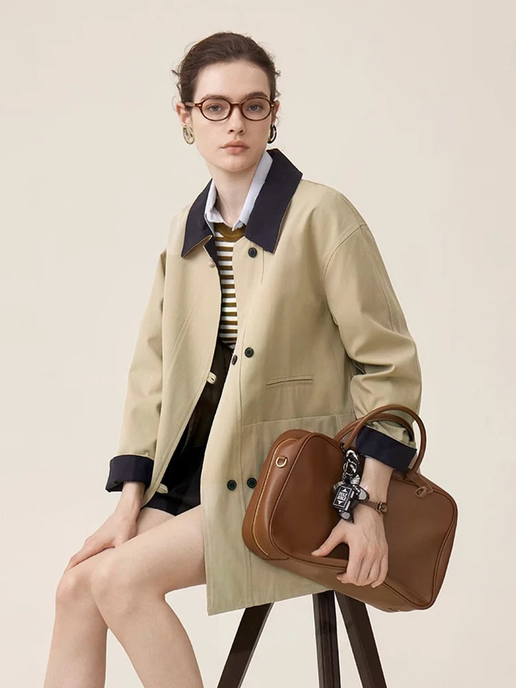 Woman holding a brown leather bag wearing a beige coat against a plain background