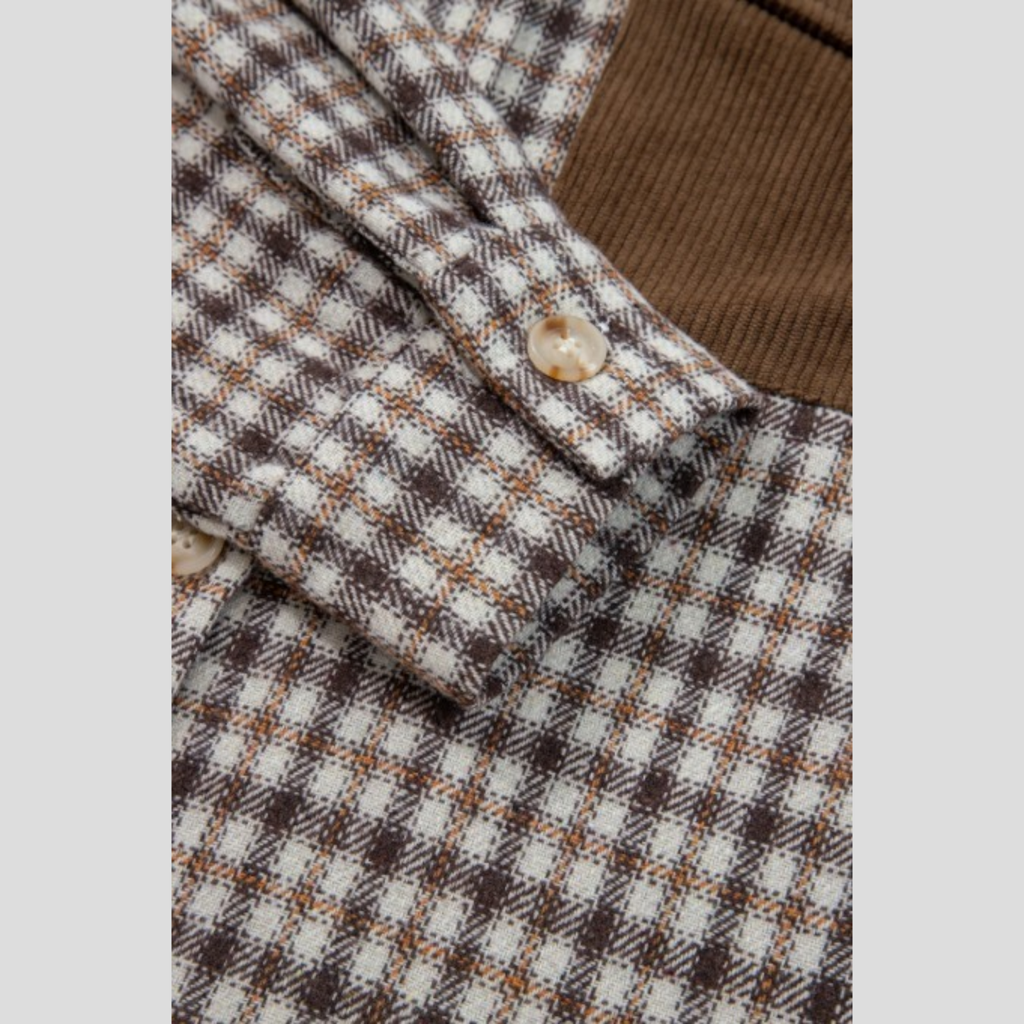 Detailed close-up of a shacket cuff, showing the button closure and the contrast between the checked fabric and corduroy material.