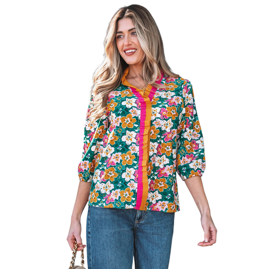 A woman wearing an emerald green floral V-neck blouse featuring distinctive magenta and ochre contrast frilled trim along the neckline and 3/4 length sleeves.