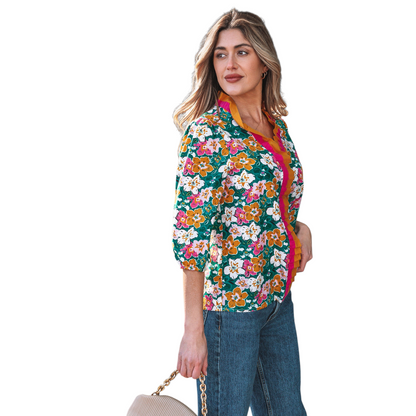 Side view of a woman wearing an emerald green floral V-neck blouse featuring distinctive magenta and ochre contrast frilled trim along the neckline and 3/4 length sleeves.