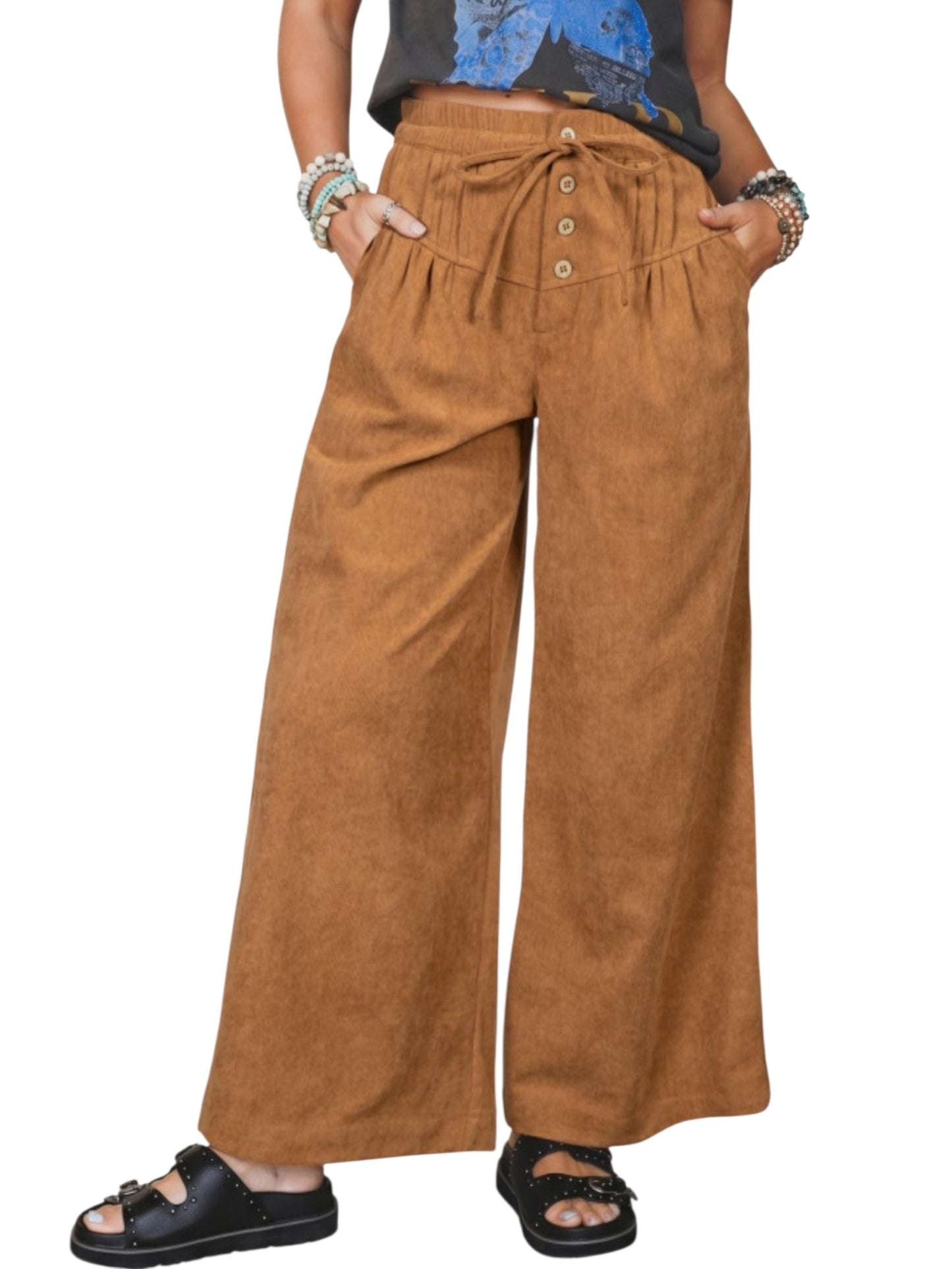 A person wearing wide-leg brown pants with a drawstring waist and button detail, paired with black sandals and bracelets, shown against a plain white background.