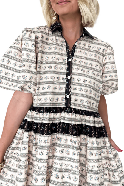 Close-up of a cream boho mini dress with floral and striped patterns, bubble sleeves, and black button detailing, showcasing intricate design and texture.