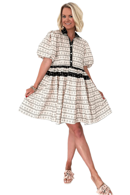 Smiling woman in a cream boho mini dress with floral and striped patterns, featuring bubble sleeves and black button details, styled with nude floral sandals for a fresh and chic look.