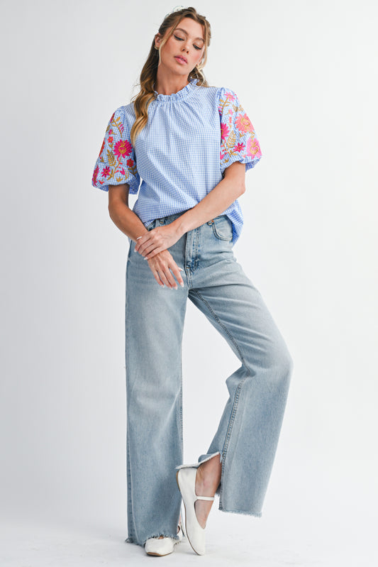 Woman wearing a blue top with floral sleeves and light blue jeans on a white background