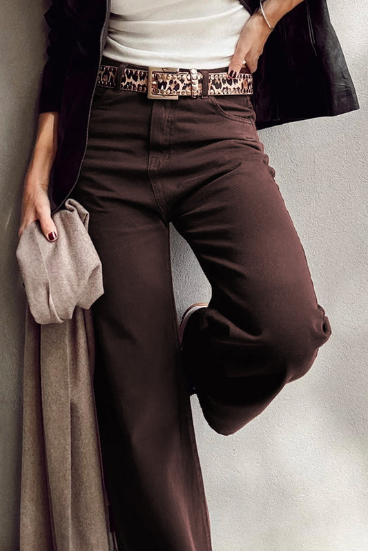 Person wearing brown pants with a leopard print belt and holding a beige jacket.