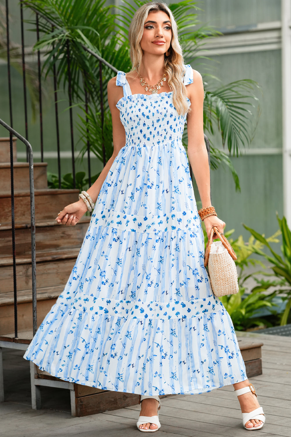 Woman wearing a blue floral dress standing outdoors with plants in the background