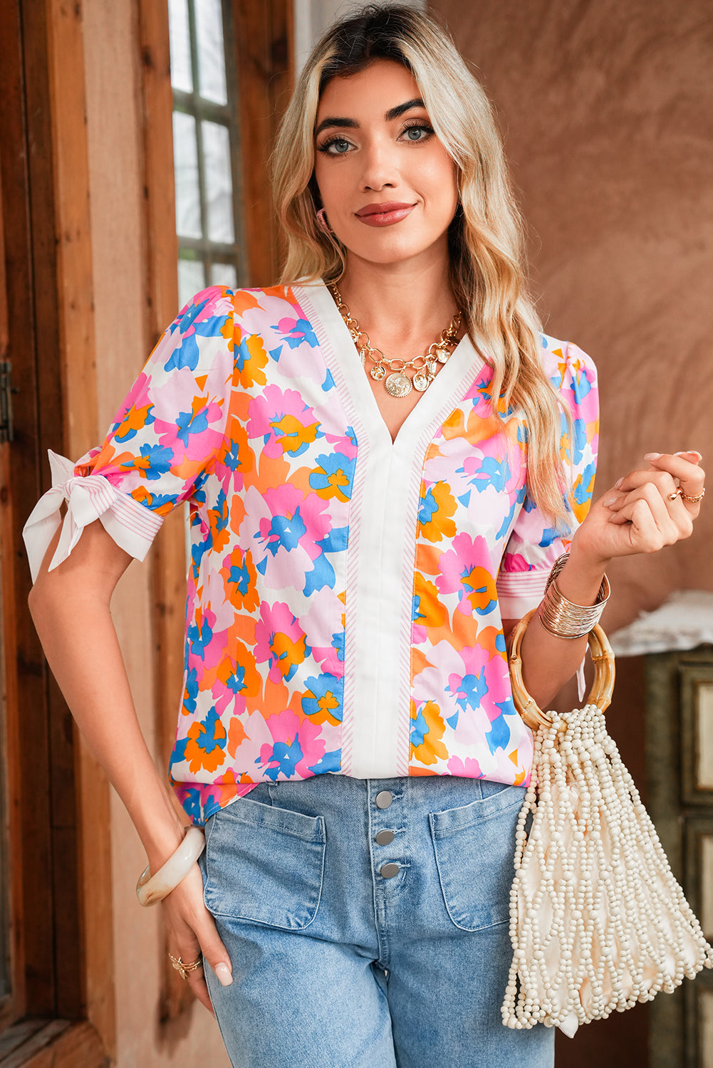 Woman wearing a colorful floral blouse and holding a beaded handbag indoors.