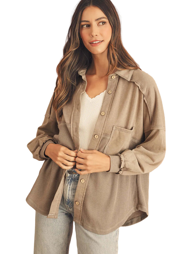 Woman wearing a beige button-up shirt over a white top and jeans on a white background