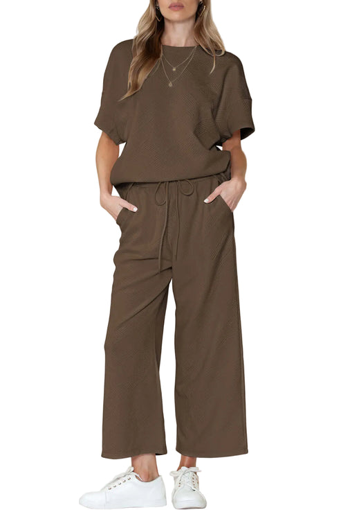 A woman wearing a green round-neck top and matching wide-leg pants with an elastic waistband, standing against a neutral background.