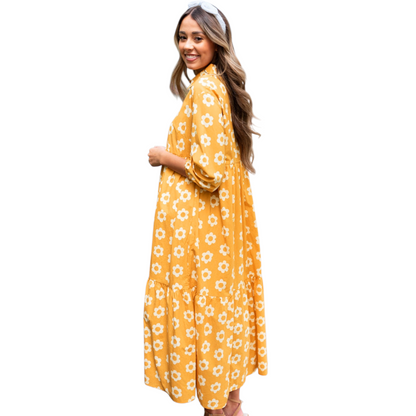 Side view of a woman wearing a yellow and white daisy print maxi dress with a collared neckline and button-down front. 