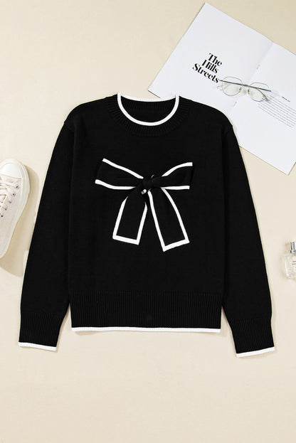 Black sweater with a white bow design on a beige surface