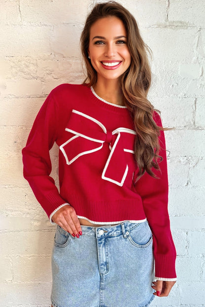 Woman wearing a red sweater with a white design against a light brick wall.