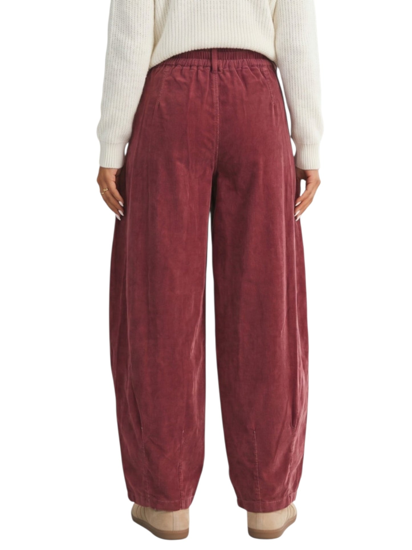 A person shown from the back wearing loose, wide-leg corduroy pants in a dusty rose or muted burgundy tone, paired with a cream ribbed sweater and tan shoes, against a plain white background.