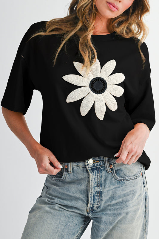 Person wearing a black sweater with a white flower design on a plain background