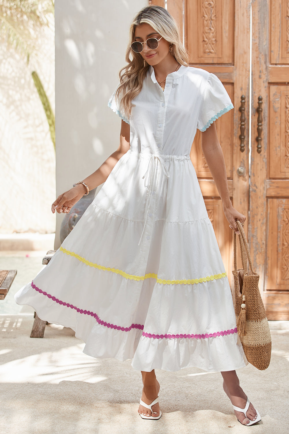 Full front view of a model standing in a white tiered shirt dress with short sleeves and a waist tie.