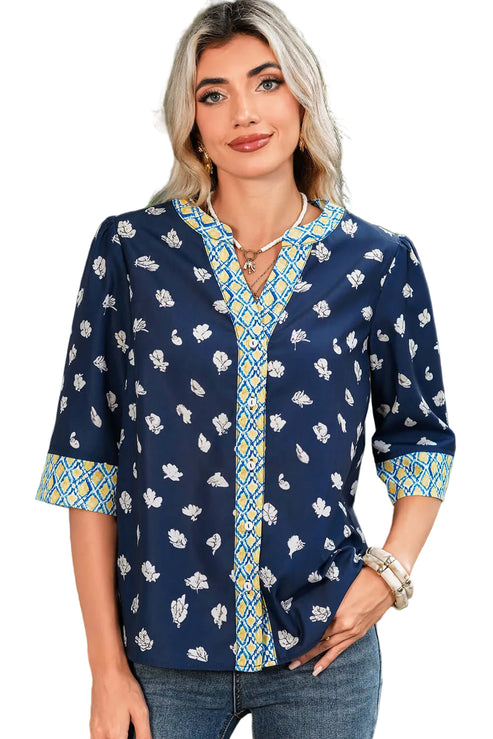 Woman wearing a navy blue patterned blouse with a blurred green outdoor background