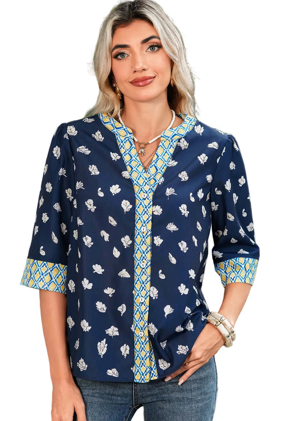 Woman wearing a navy blue patterned blouse with a blurred green outdoor background