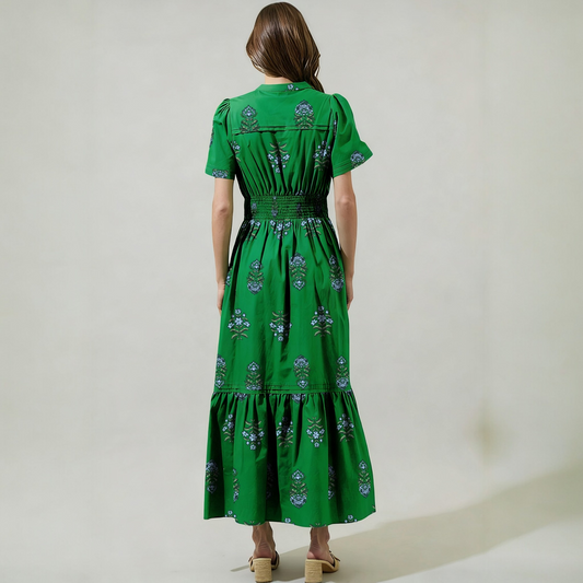 Rear view of a green embroidered maxi dress highlighting the shirred elastic waistband and tiered ruffle hem silhouette.