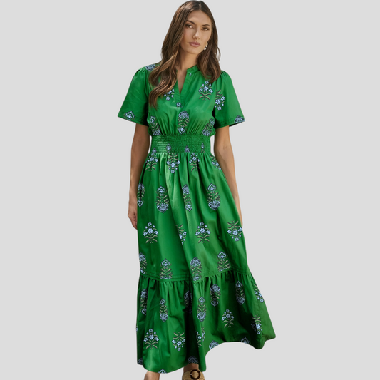 Front view of a model wearing a green cotton-blend maxi dress with blue floral embroidery, a shirred high waist, and a split neckline.