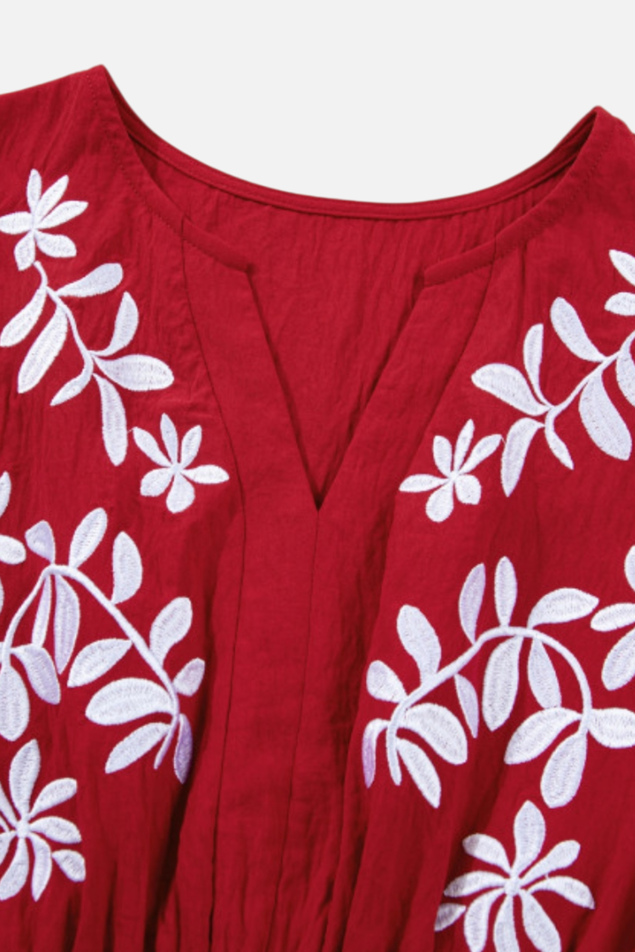 A close-up shot of the exquisite white contrast floral embroidery and notched V-neckline on the crinkle-textured burgundy fabric.