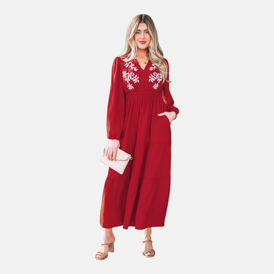 A full-length front view of a model wearing a burgundy tiered maxi dress featuring intricate white floral embroidery on the bodice and a flattering cinched waist.