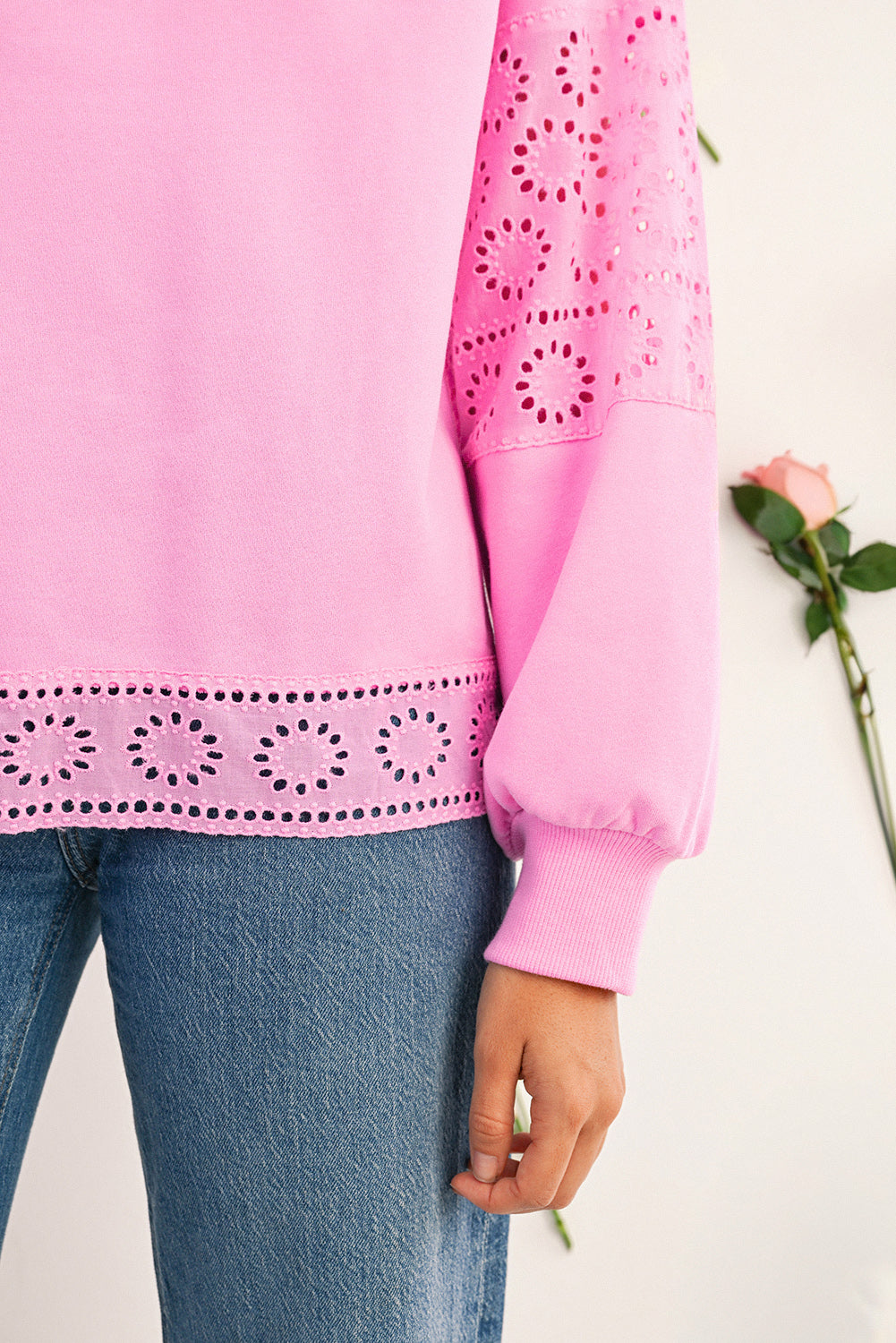 Pink sweater with eyelet details worn by a person, against a white background.