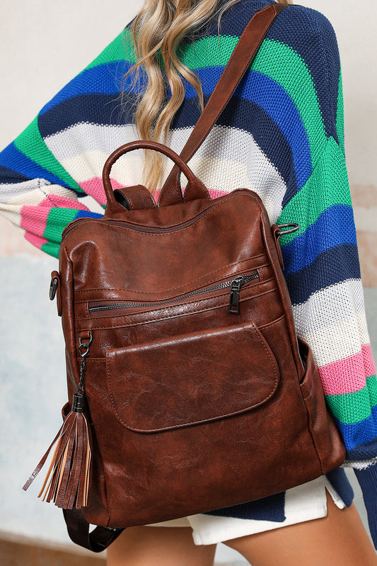 Brown leather backpack with tassel held by a person wearing a colorful striped sweater.