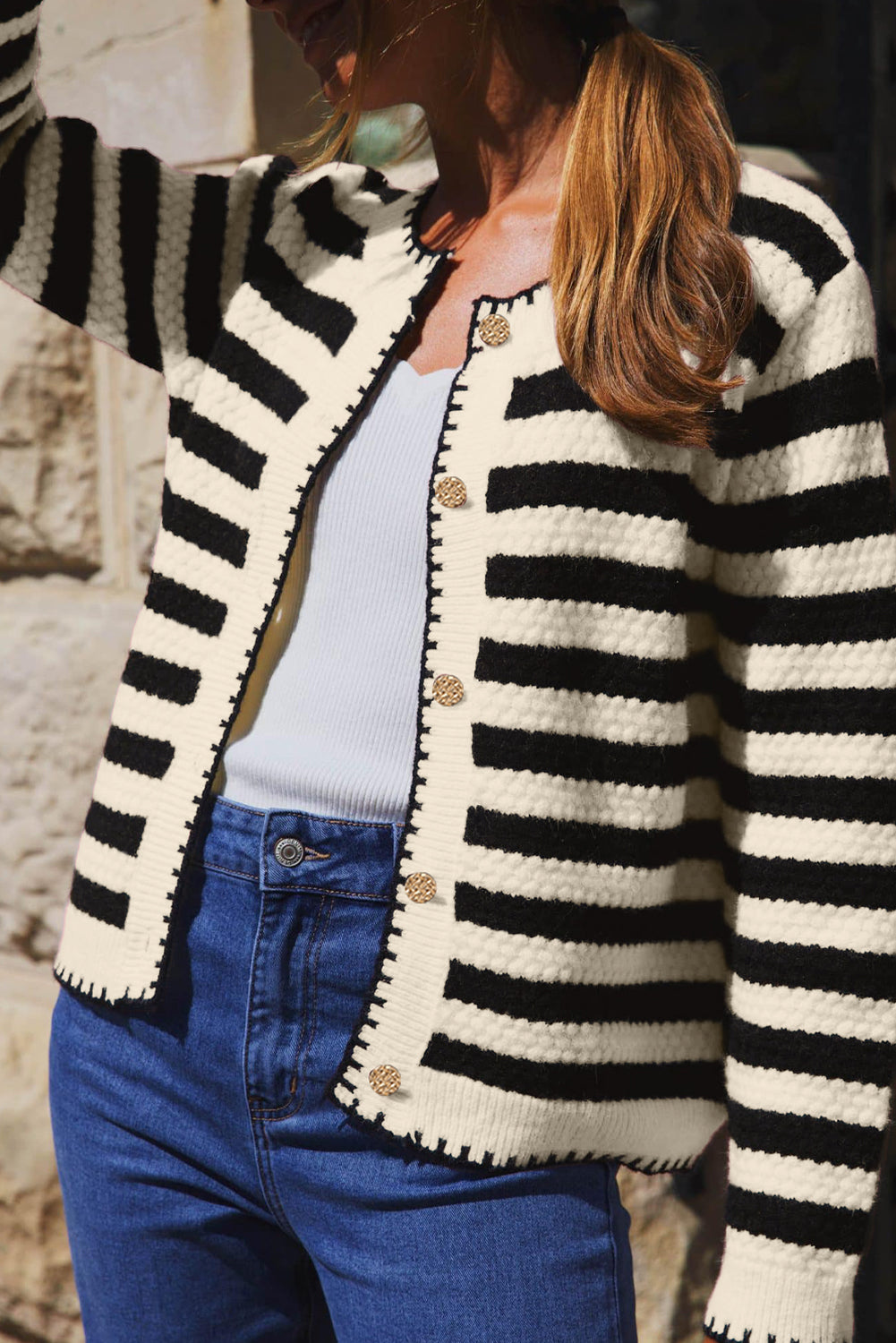 Person wearing a black and white striped cardigan with a stone wall background