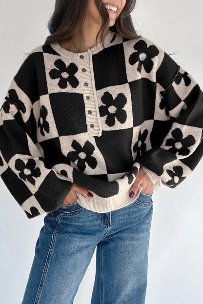 Person wearing a black and white checkered sweater with floral patterns and blue jeans on a light gray background