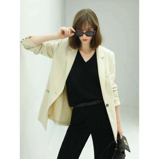 Woman wearing a beige blazer over a black top with sunglasses on a light gray background