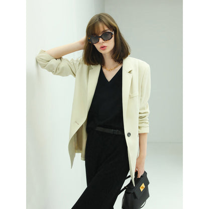 Woman wearing a beige blazer over a black outfit with sunglasses against a light background