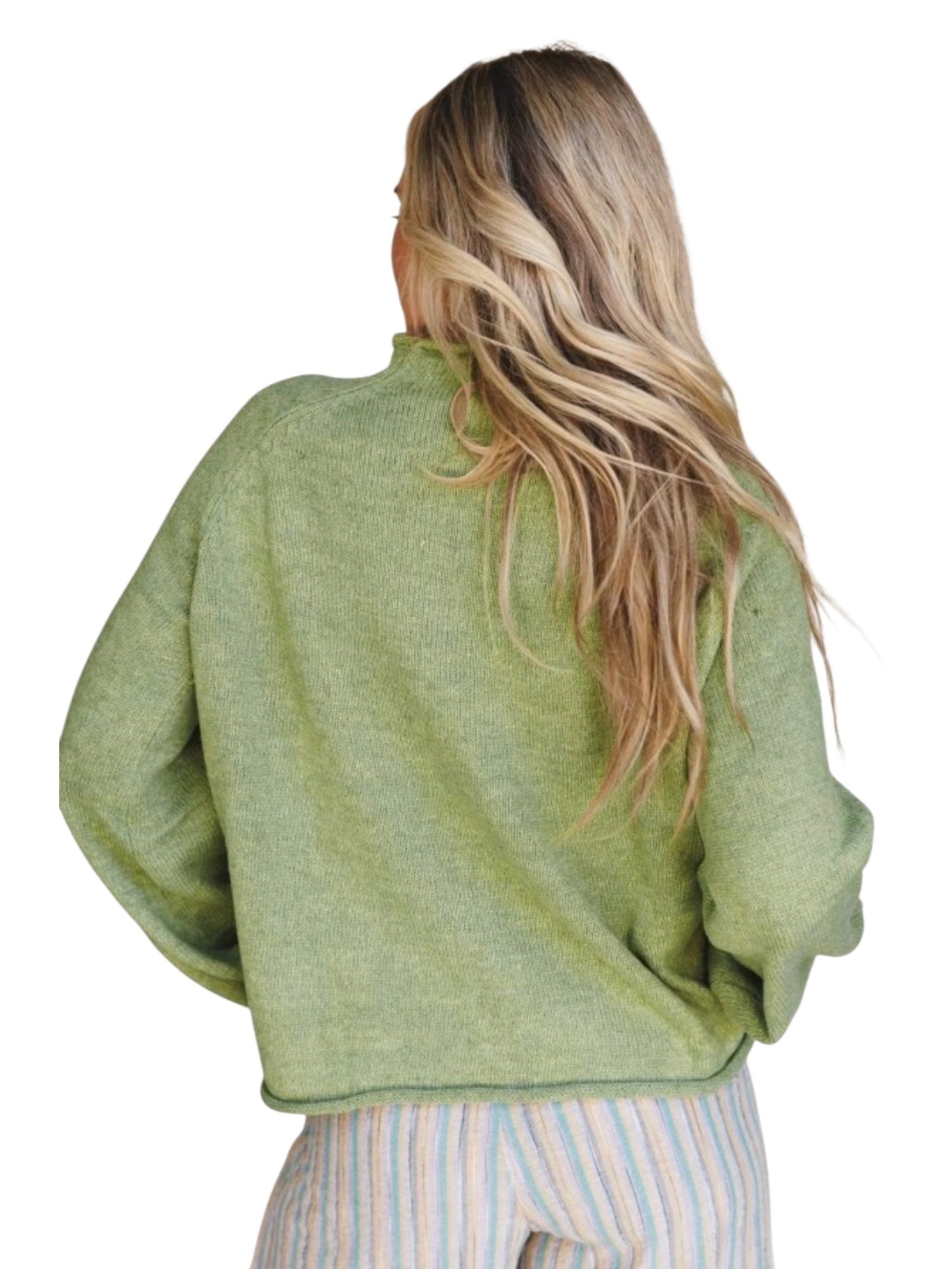A woman with long blonde hair is shown from behind wearing a light sage green knit sweater and striped pants against a plain white background.