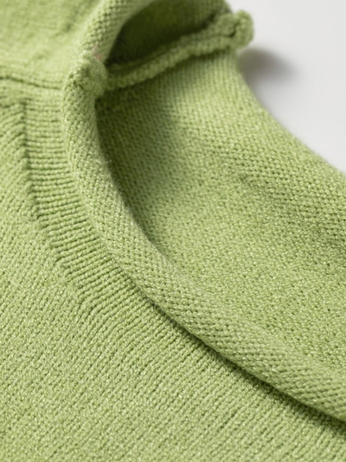 Close-up of a light green knit garment showing the ribbed collar and fine fabric texture against a white background.