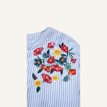 Close-up of intricate red and yellow floral embroidery on a blue pinstripe 100% polyester fabric.