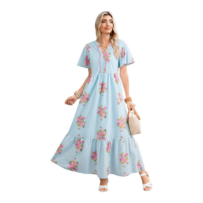 A woman wearing a light blue floral maxi dress with pink rose patterns, featuring flutter short sleeves and a notched neckline.