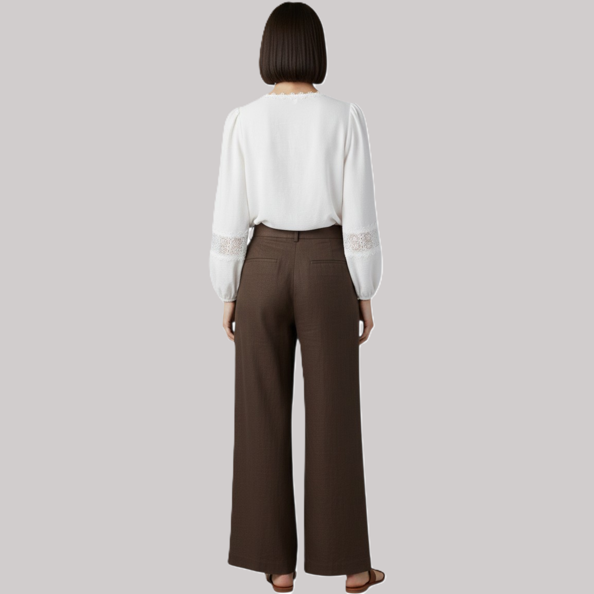 Person wearing a white blouse with lace sleeves and brown pants on a gray background