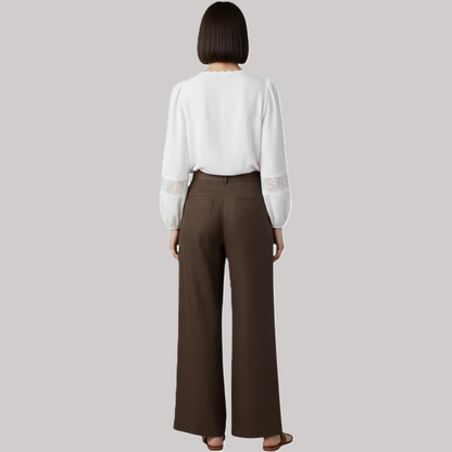 Person wearing a white blouse with lace sleeves and brown pants on a gray background