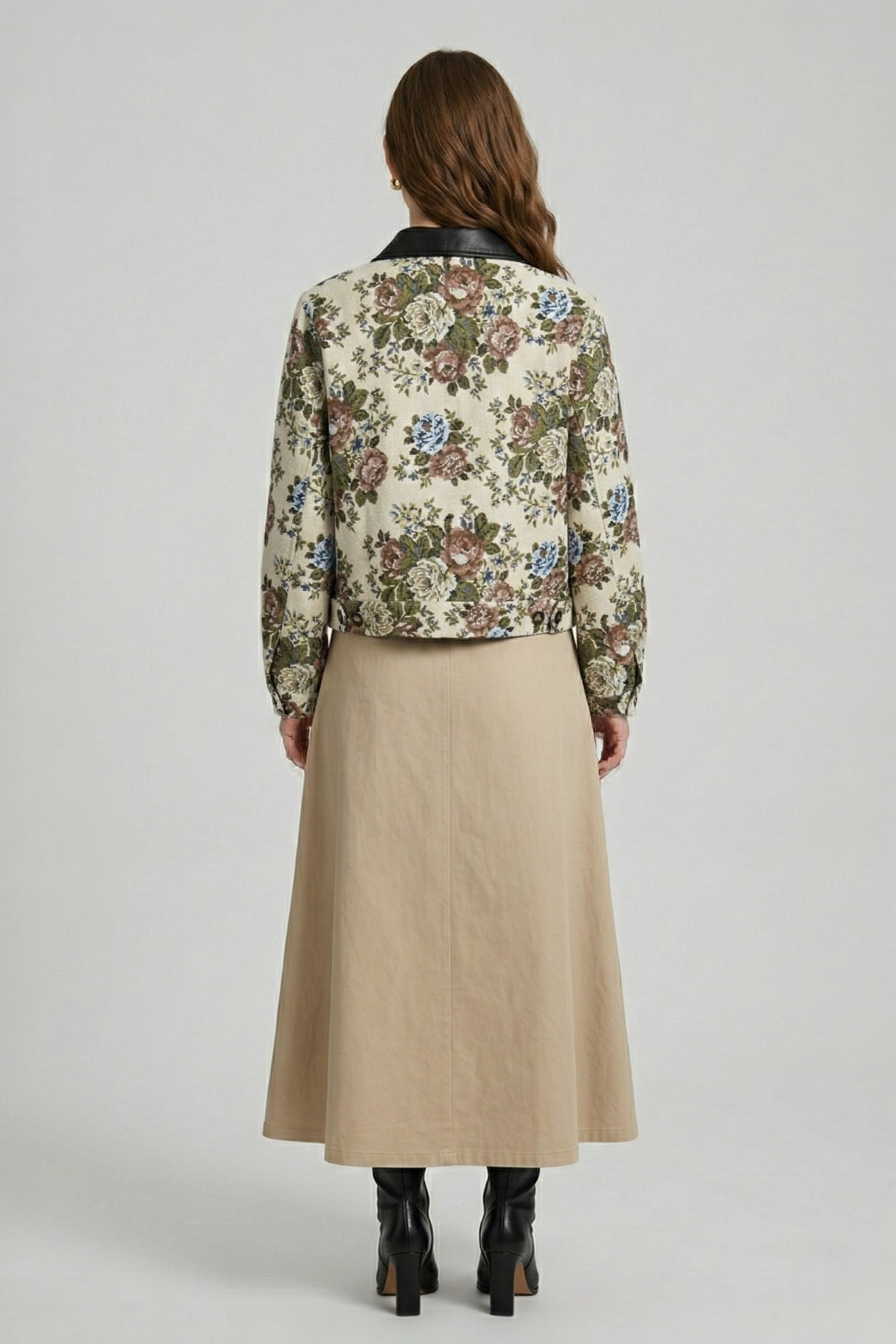 Back view of a  model wearing a beige floral jacquard cropped jacket with a black collar, styled with a matching dress and black boots.