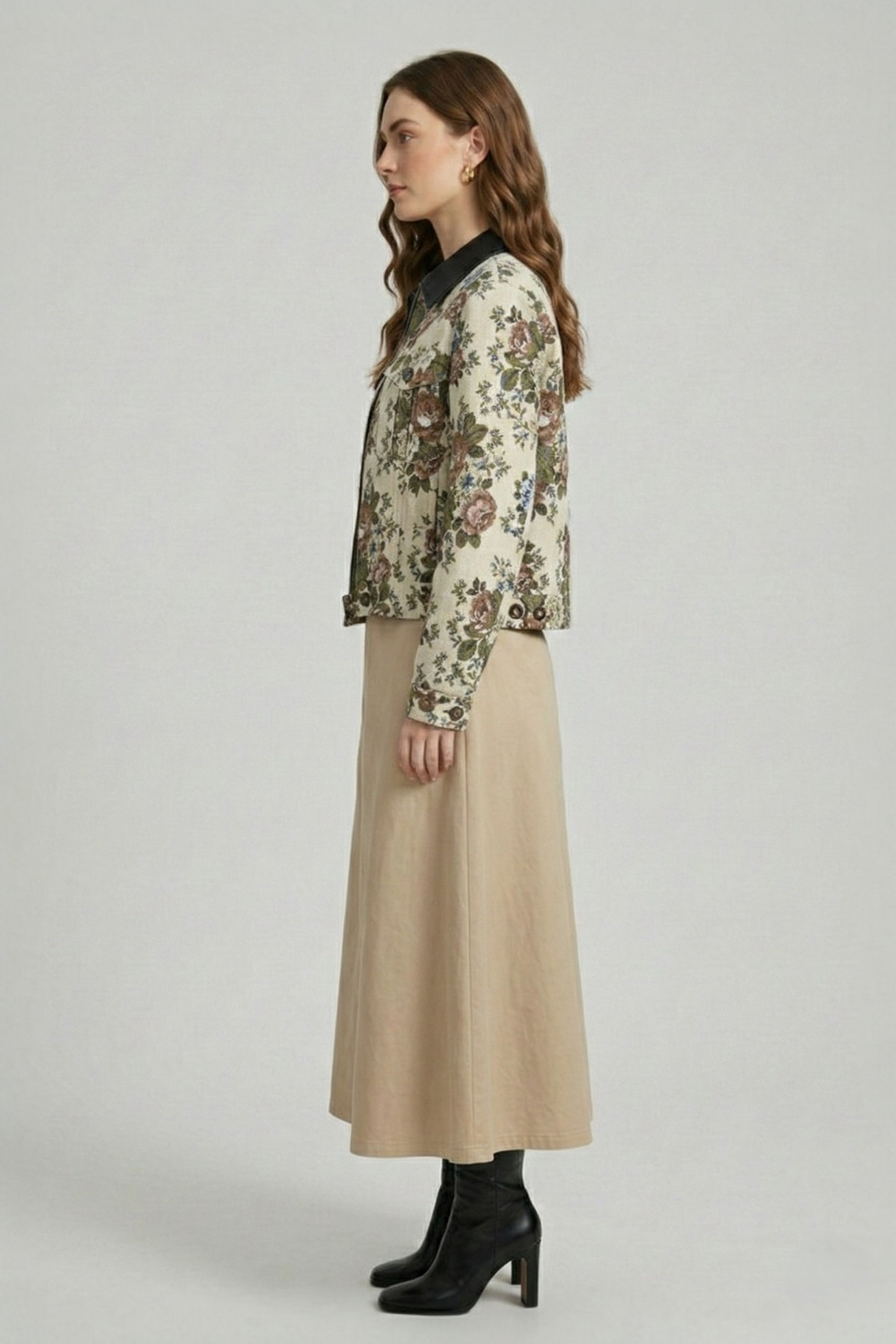 Side view of a model wearing a beige floral jacquard cropped jacket with a black collar, styled with a matching dress and black boots.